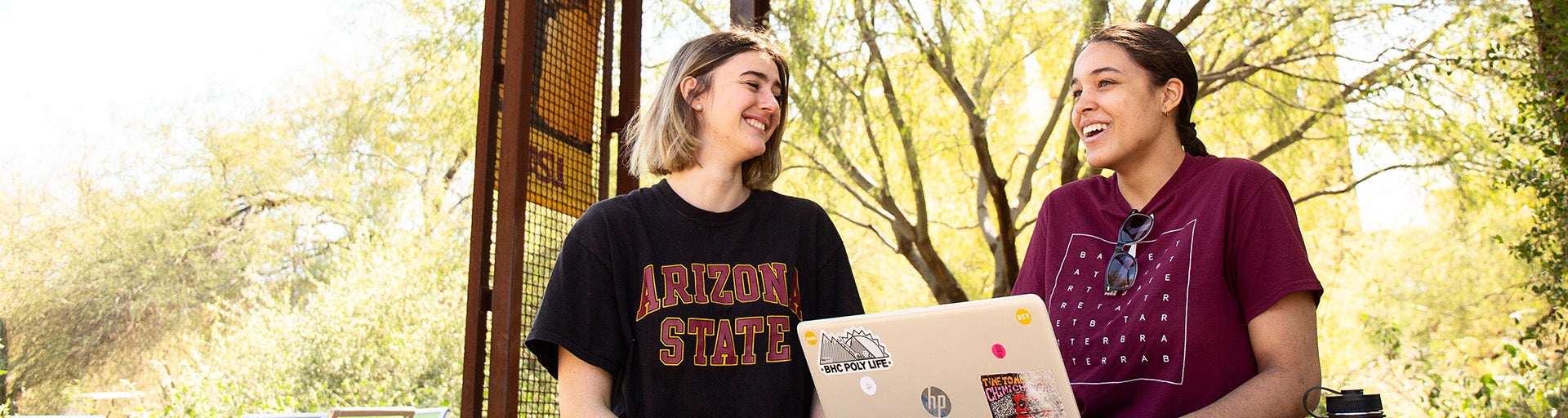 Two Barrett students having a conversation while using a laptop outside on campus