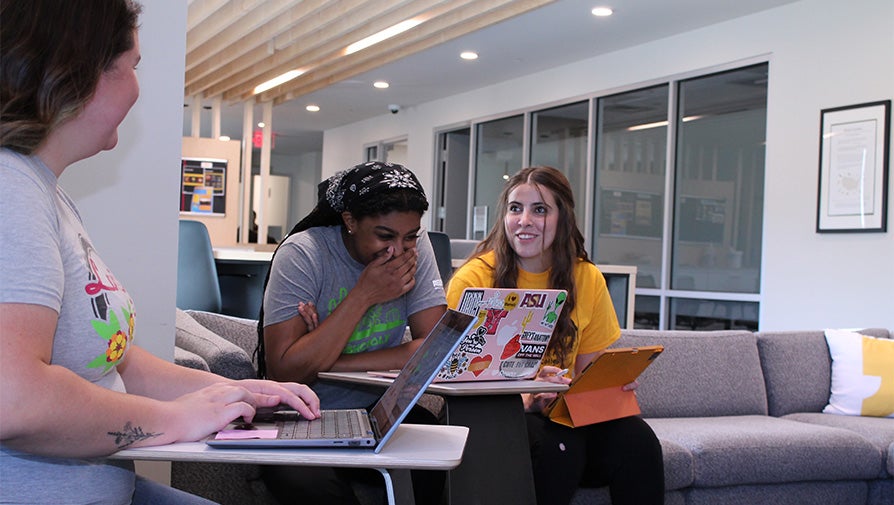 Three students having a conversation and using their laptops at the Barrett Suite