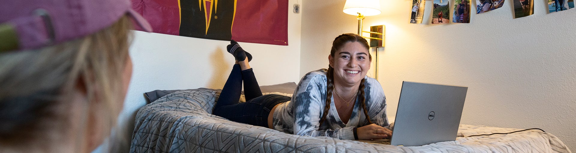 Female student talking to another student in dorm room while using laptop